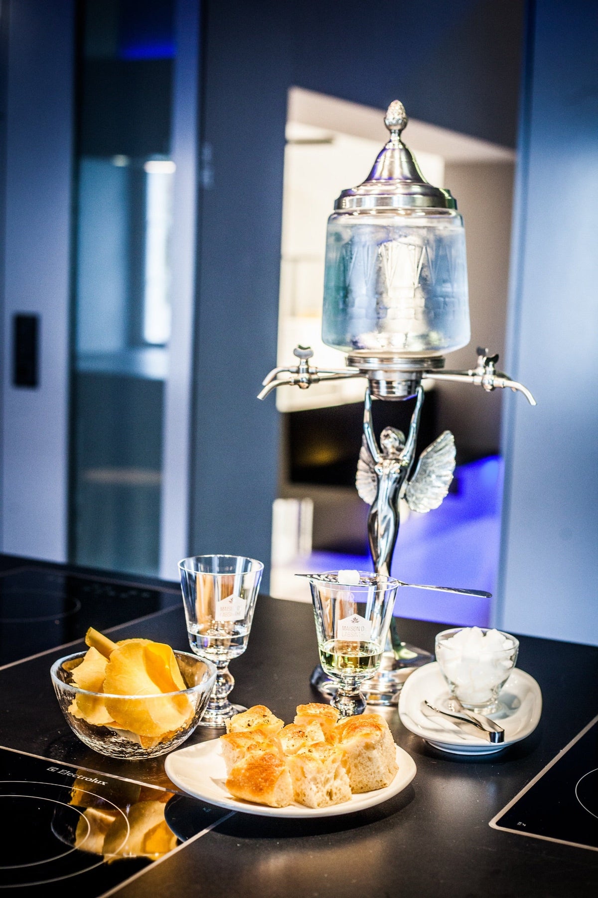 An absinthe fountain beside two glasses of louched absinthe, sugar cubes and bites for the apéritif