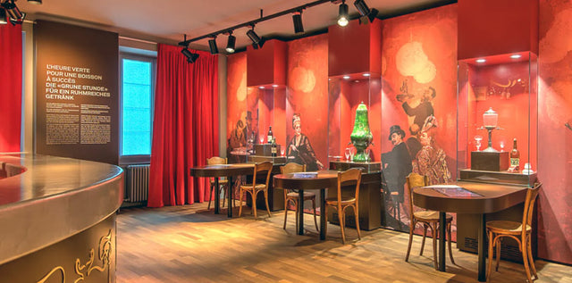 The Heure Verte bar room at Maison de l'Absinthe, with its red walls, period murals and absinthe fountain
