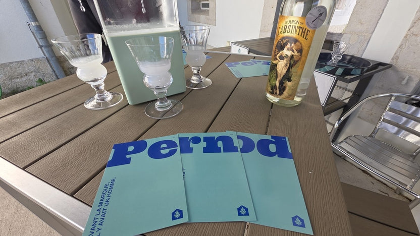 Three louched absinthes in Pontarlier glasses beside a carafe and the exhibition brochures
