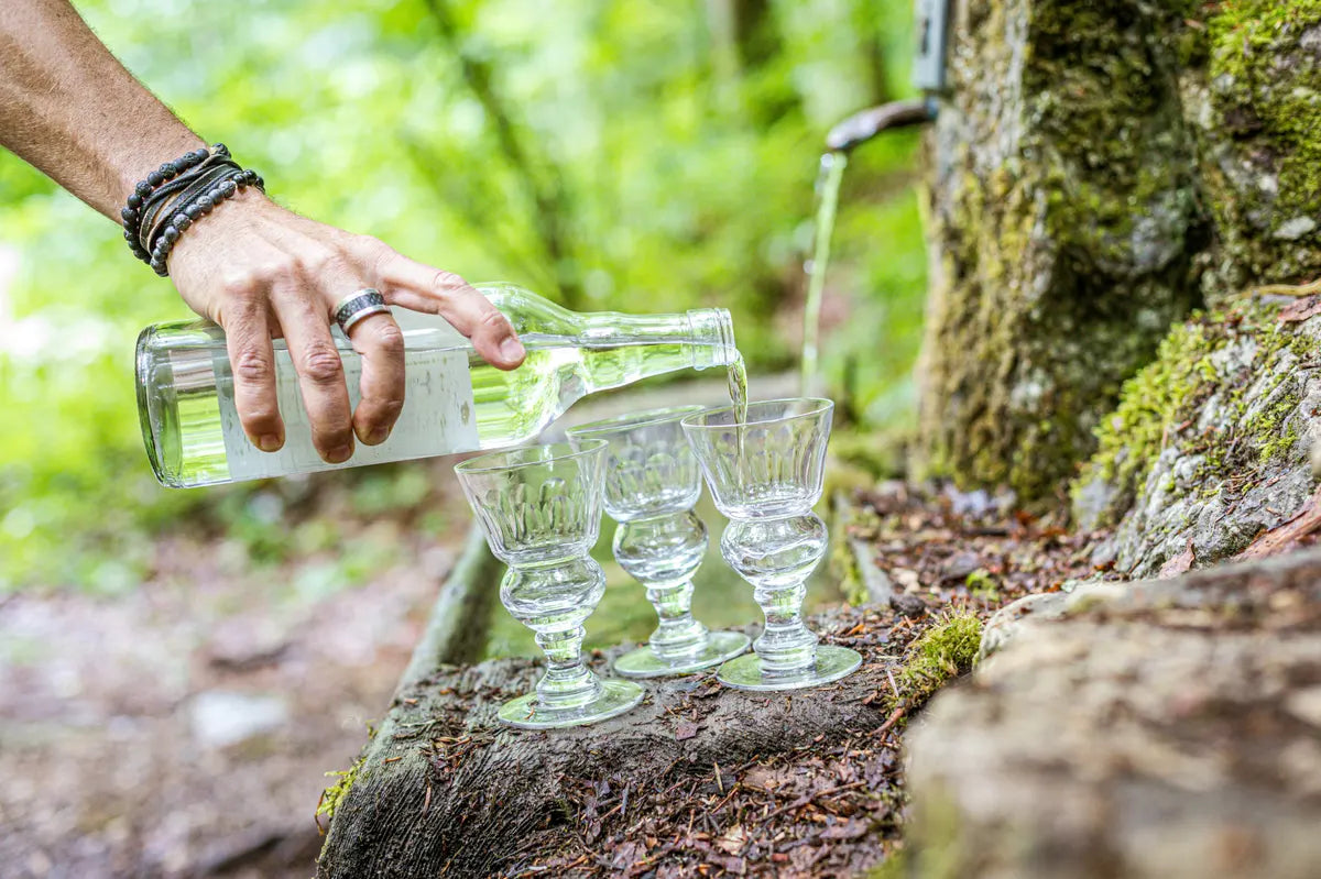 Absinthe poured into three Pontarlier glasses beside a forest spring in the Val-de-Travers