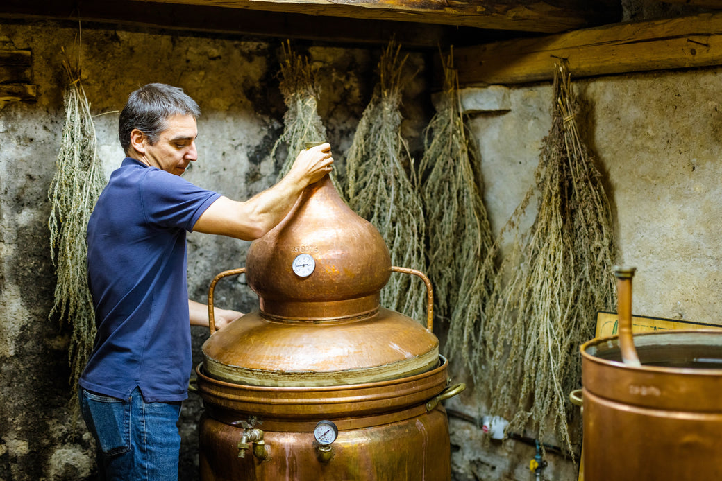 Absinthe distillateur working beside copper alembics during a production demonstration