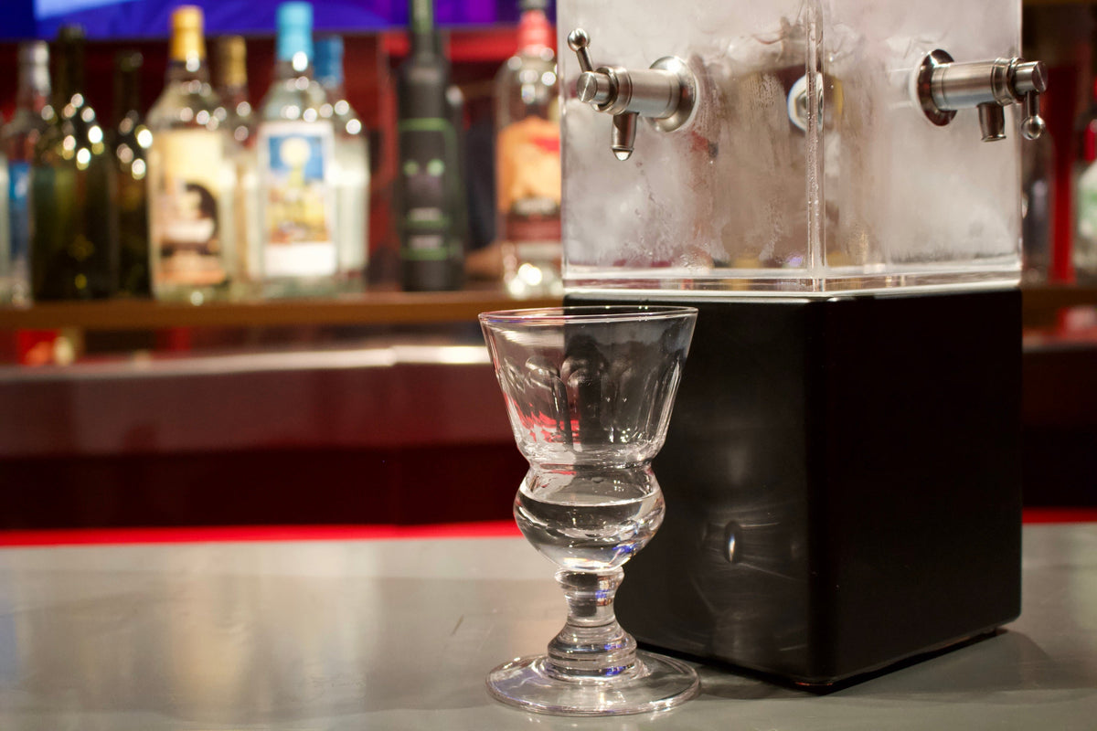 Single absinthe glass beside an acrylic drip fountain at the museum tasting bar