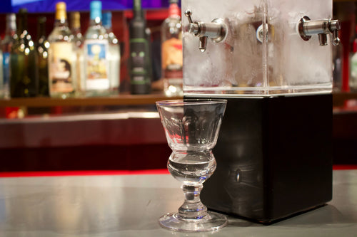 Single absinthe glass beside an acrylic drip fountain at the museum tasting bar